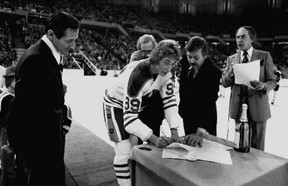 Wayne Gretzky signs a twenty one year contract with the Edmonton Oilers, then of the World Hockey Association, at centre ice Jan. 26 1979, before a game against Cincinnati Stingers. Helping Gretzky sign, on his eightteen birthday is Oilers general manager Larry Gordon. Standing on the left is Walter Gretzky, Wayne's father. Photo by Ken Orr, Edmonton Journal file