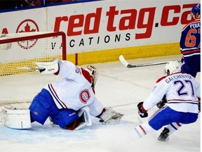 Edmonton Oilers Benoit Pouliot (right) scores on Montreal Canadiens goalie Dustin Tokarski (left) during first period NHL game action in Edmonton on October 27, 2014, as Canadiens Alex Galchenyuk (#27) watches helplessly.