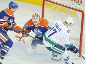 Goalie Ben Scrivens, middle, of the Edmonton Oilers, watches the puck sail past Radim Vrbata, right, of the Vancouver Canucks at Rexall Place in Edmonton on Friday, Oct. 17, 2014.