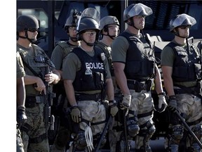 Police in riot gear watch protesters in Ferguson, Mo. on Wednesday, Aug. 13, 2014.