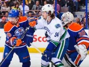 Mark Arcobello #26 and Ben Scrivens #30 of the Edmonton Oilers defend net against Kellan Lain #54 of the Vancouver Canucks during an NHL game at Rexall Place on January 21, 2014 in Edmonton, Alberta, Canada.