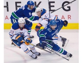 Vancouver Canucks defenceman Dan Hamhuis (2) and teammate Brad Richardson (15) fight for control of the puck with Edmonton Oilers centre Ryan Nugent-Hopkins (93) and Taylor Hall (4) during the second period of NHL action in Vancouver on Saturday, Oct. 11, 2014.