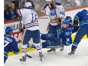 Vancouver Canucks’ Ryan Stanton (18) is tripped up by Edmonton Oilers’ Teddy Purcell (16) while battling for control of the puck with Oilers’ Jordan Eberle (14) during the second period of a preseason NHL hockey game in Vancouver, B.C., on Oct. 4, 2014.
