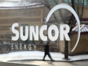 A pedestrian is reflected in a Suncor Energy sign in Calgary, Monday, Feb. 1, 2010. Suncor Energy Inc. (TSX:SU) is reducing its workforce by 1,000 and cutting $1 billion from its capital budget in response to plummeting crude oil prices.