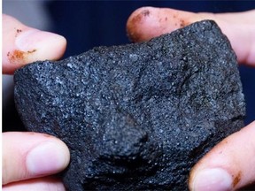 In this September 2013 file photo, Aaron Fairbrother, an interpreter with the Oilsands Discovery Centre, holds a clump of petroleum coke from oilsands bitumen upgrading in Fort McMurray.