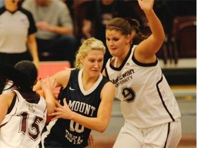 MacEwan Griffins guard Kendall Lydon, left, and forward Megan Wood, right, defend against Mount Royal Cougars guard Florence Jennings during Canada West women’s basketball action at MacEwan’s City Centre Campus Gym in Edmonton on Nov. 7, 2014.