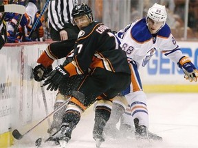 Andrew Cogliano of the Anaheim Ducks turns to look for the puck while getting checked by Edmonton Oilers defenceman Brandon Davidson during Wednesday’s National Hockey League game at Anaheim, Calif.