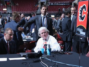 Calgary Flames GM Brad Treliving and POHO Brian Burke are photobombed by some random dude while discussing strategy at the draft table.