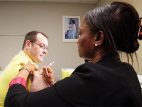 Dr. Christopher Sikora, medical officer of health for the Edmonton Zone of Alberta Health Services, gets a flu shot from RN Benedicta Kuibi at the Woodcroft Public Health Centre on Oct. 20, 2014, in Edmonton. Nearly 100 Albertans have died from flu this season, new statistics show.