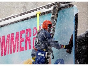 An outdoor sign installer puts up a new sign on a downtown Edmonton billboard as snow flurries fell throughout the day on Wednesday.