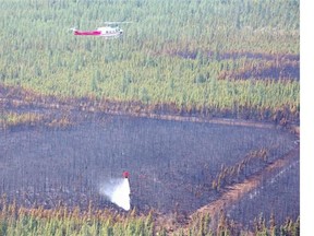 A helicopter drops a bucket of water on a hot spot along the edge of a contained wildfire approximately 22 kilometres east of Slave Lake Alta. on May 27, 2015.