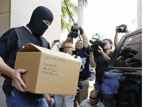 A masked FBI agent carries a box from the headquarters of CONCACAF after it was raided on May 27, 2015 in Miami Beach, Fla. The raid is part of an international investigation of FIFA, where nine FIFA officials and five corporate executives were charged with racketeering, wire fraud and money laundering conspiracies.