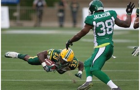 Edmonton Eskimos’ Shakir Bell (33) is tripped up by Tristan Jackson (38) of the Saskatchewan Roughriders during pre-season Canadian Football League action in Fort McMurray on June 13, 2015.