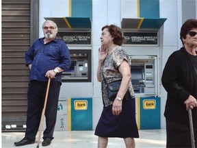 People stand by Greece national bank’s empty ATMs in central Athens on June 29, 2015, as Greece ordered its banks to shut for one week and imposed capital controls today, sending markets tumbling after its citizens emptied ATMs on the eve of a potentially disastrous default.