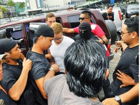 Saskatchewan resident Lindsey Petersen, centre, is escorted by police as he arrives at court on Borneo island, Malaysia, on Friday, June 12, 2015. Petersen and his sister Danielle were among 10 people who stripped naked and took photos on Mount Kinabalu on May 30.