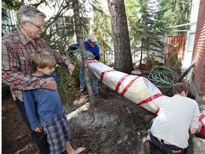 Walter Baydala holds his grandson Phoenix, 8, watching as Brendan Griebel (R), director of the Inuit Heritage organization and Gordon Baergen remove a historic caribou skin kayak from the basement window of Walter’s house where it has been stored for nearly 50 years in Edmonton, August 17, 2015. It is being returned to its home in the Nunavut community of Kugluktuk.