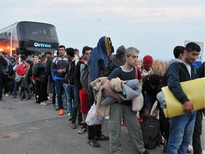 A group of Middle-Eastern migrants gets off the bus on their way to cross the Croatian-Hungarian border in the village of Baranjsko Petrovo Selo, near North-Eastern Croatian town of Beli Manastir, on Sept. 24, 2015. Watching them are Hungarian military and border police.