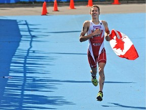 Canada's Tyler Mislawchuk being cheered as fans shadows are cast on the finish line from the bleachers, on his way to win the bronze medal in the 4 x mixed relay U23 and junior event at the World Triathlon Series Grand Final at Hawrelak Park in Edmonton, Sept. 1, 2014.