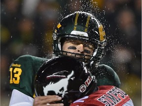 Edmonton Eskimos quarterback Mike Reilly gets hit by Calgary Stampeders linebacker Juwan Simpson, shaking off the rain from his helmet during a Canadian Football League game at Commonwealth Stadium  on Sept. 12, 2015.