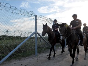 Hungarian officers of the mounted police unit patrol the newly set up fence on the border with Serbia as refugees from Middle Eastern countries approach Serbia-Hungary border on foot near the Northern-Serbian town of Horgos, on Sept. 14, 2015.