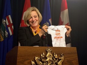 Premier Rachel Notley holds up a onesie emblazoned with a quote from former federal NDP Leader Jack Layton. The onesie is destined for Calgary-Varsity NDP MLA Stephanie McLean, who will deliver her first child in February - becoming the first sitting MLA in Alberta's history to deliver a baby during her term in office.