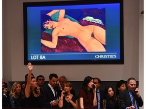 Bid takers stand in front of a video screen with  Amedeo Modigliani's Nu couche during the Artist Muse: A Curated Evening Sale on Monday at Christie's New York. The painting sold for $170,4. million US.