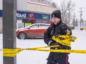 A police officer removes crime-scene tape at a Mac's convenience store in Edmonton on Friday, Dec. 18, 2015. Two men, both Mac's employees, were shot and killed early Friday during separate holdups.
