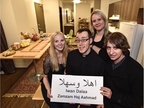 Holding a welcome sign, Father Glenn McDonald, minister Theresa Robinson, students Danika Jurczak (L) and Simon Kaczyk (R) in the room where a family of four Syrian refugees they're sponsoring will stay temporarily at St. Joseph's College women's residence in Edmonton.