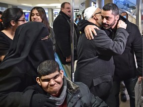 Hussein Jomaa (R), chairman of the Edmonton Islamic Relief Centre, on Tuesday greets Syrian Refugees, Abdul Salam Kamali with his wife Fatima and son Anas (L), who is in a wheelchair.