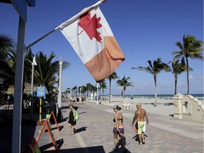 In this Monday, Nov. 23, 2015 photo, a Canadian flag flies as people walk along the boardwalk in Hollywood, Fla. Visits by the United States' largest supply of international visitors from Canada are expected to be down by 8 percent this year due to the weak Canadian dollar.