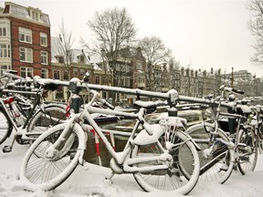 Snow-covered bikes obscure this canal in Amsterdam in winter.