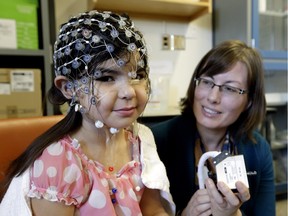 Helping with research at the University of Alberta is Kaia Anderson-Fillier, 4, whose sensor cap will record her brain activity  while she plays a computer video game.  With her is researcher Sandra Wiebe, associate professor of psychology, who is working with others on the effects of screen time on early childhood development.  John Bergeron is advocating for federal funding to make Alberta a centre for Canadian research.