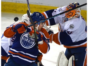 The puck flying behind Edmonton Oilers Matt Hendricks (23) and  New York Islanders Johnny Boychuk (55) as goalie Jaroslav Halak (41) goes after it during NHL action at Rexall Place in Edmonton, February 28, 2016.