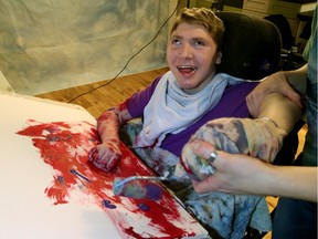 Nathan Devlin smiles as he paints in his art studio that is inside his house with the help from his assistant Renee Laporte on Monday Feb. 1, 2016.