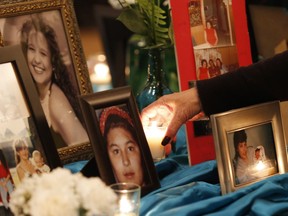 A woman places a candle beside portraits of murdered and missing women on a memorial table at the 2nd National Roundtable on Missing and Murdered Indigenous Women and Girls in Winnipeg on Feb. 25, 2016.