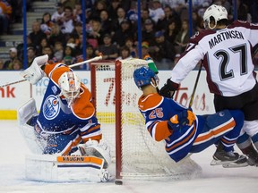 Goalie Laurent Brossoit (1) of the Edmonton Oilers makes a save while Darnell Nurse (25) of the Oilers falls to the ice after being struck by Andreas Martinsen (27)playing against the Colorado Avalanche at Rexall Place  in Edmonton on March 20, 2016.