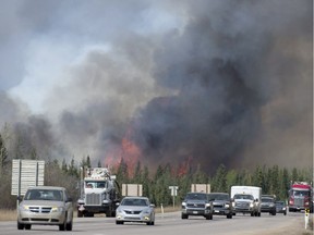 A convoy of cars and trucks pass wildfires as they are evacuated from Fort McMurray, Alta., on highway 63 south of the city on Saturday, May 7, 2016.