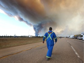 A man wearing fire retardant clothing walks up to a road block on Highway 63 as smoke rises from a forest fire near Fort McMurray, Alberta on May 6, 2016.