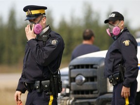 Two police officers wear masks to protect themselves from falling ash in the air at a road block on Alberta Highway 63 near Fort McMurray on May 5, 2016.
