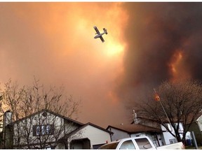 Smoke fills the air as a small plane flies overhead in Fort McMurray, Alberta on Tuesday May 3, 2016. Raging forest fires whipped up by shifting winds sliced through the middle of the remote oilsands hub city of Fort McMurray Tuesday, sending tens of thousands fleeing in both directions and prompting the evacuation of the entire city.