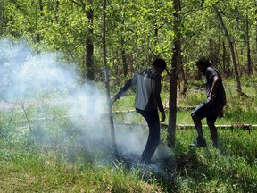 Fort McMurray evacuees, Cosmas Thebe (L) and his son Bongi Thebe, try to stomp out a hot spot during a wild land fire in Buena Vista Park in Edmonton May 8, 2016.