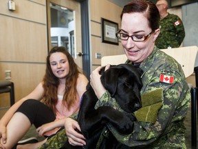 Ortona, National Service Dogs' puppy-in-training, cuddles with his handler Capt. Donna Riguidel as her daughter, Darby Riguidel, 13, looks on at CFB Edmonton on June 6, 2016. Ortona is exploring the world of the Canadian Armed Forces and sharing his adventures online.