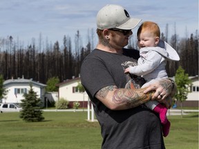 Charred trees are visible in the background as Brandon Gourlay and his seven month-old daughter Zylah Marie Gourlay a walk through the Morgan Heights (Timberlea) neighbourhood, in Fort McMurray on Tuesday June 14, 2016.