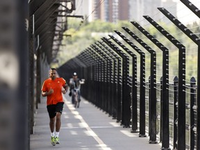 A runner and cyclists crosss the west sidewalk of the High Level Bridge.