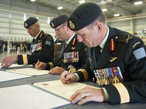 Brig.-Gen. Simon Hetherington (right), new commander of 3rd Canadian Division; Lt.-Gen. Marquis Hainse (centre), chief of the army staff; and Brig.-Gen. Wayne Eyre, outgoing commander of 3rd Canadian Division, sign documents during the change of command signing ceremony at Edmonton Garrison July 11, 2016.