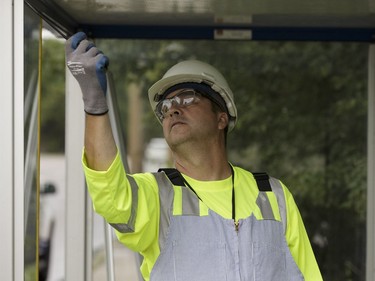 Edmonton Transit System utility worker Robert Young cleans a broken glass panel while replacing a panel with coworker Pono Vey at a bus shop on 107 Avenue near 120 Street in Edmonton, on Wednesday, July 20, 2016.