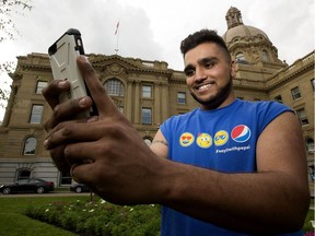 Simrit Birdi poses for a photo while playing the video game Pokemon Go on his cellphone at the Alberta legislature grounds in Edmonton.