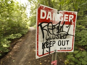 A sign covered in graffiti warns of a destroyed trail in Forest Heights Park in Edmonton.