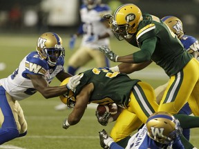 Edmonton Eskimos running back John White (30) is tackled by Winnipeg Blue Bombers' Kevin Fogg (23) during CFL action at The Brick Field at Commonwealth Stadium in Edmonton, on July 28, 2016.