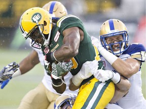 Winnipeg Blue Bombers' Ian Wild (38) and Taylor Loffler (16) tackle Edmonton Eskimos Patrick Watkins (9) during first half CFL action in Edmonton on  July 28, 2016.